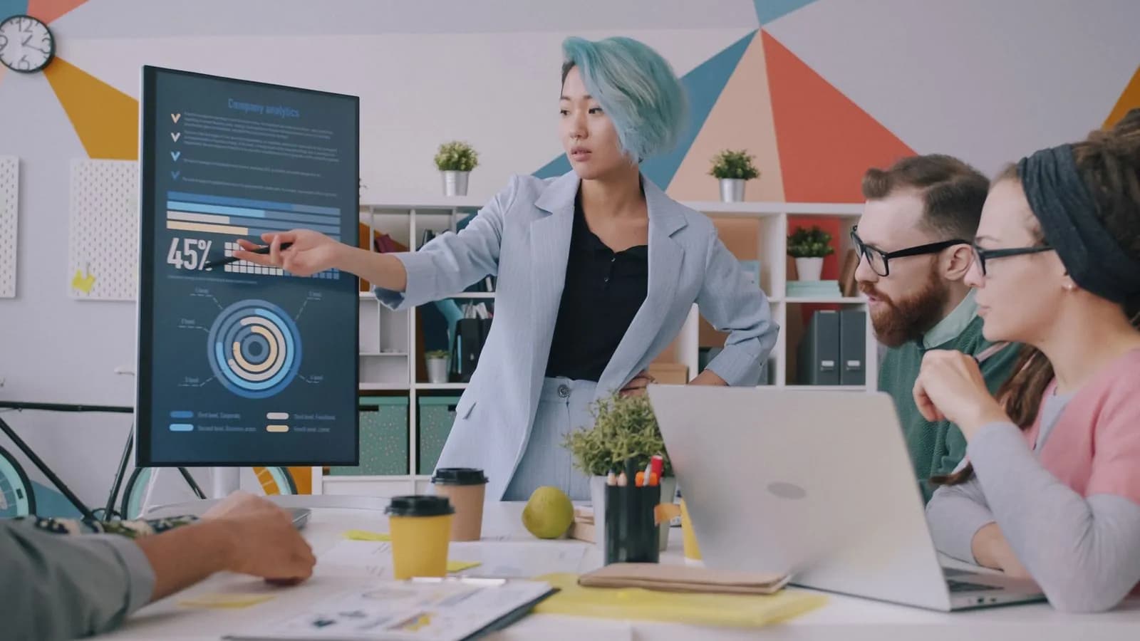 Une équipe échange autour d’ordinateurs portables pendant qu’une collaboratrice présente des indicateurs à l’écran.